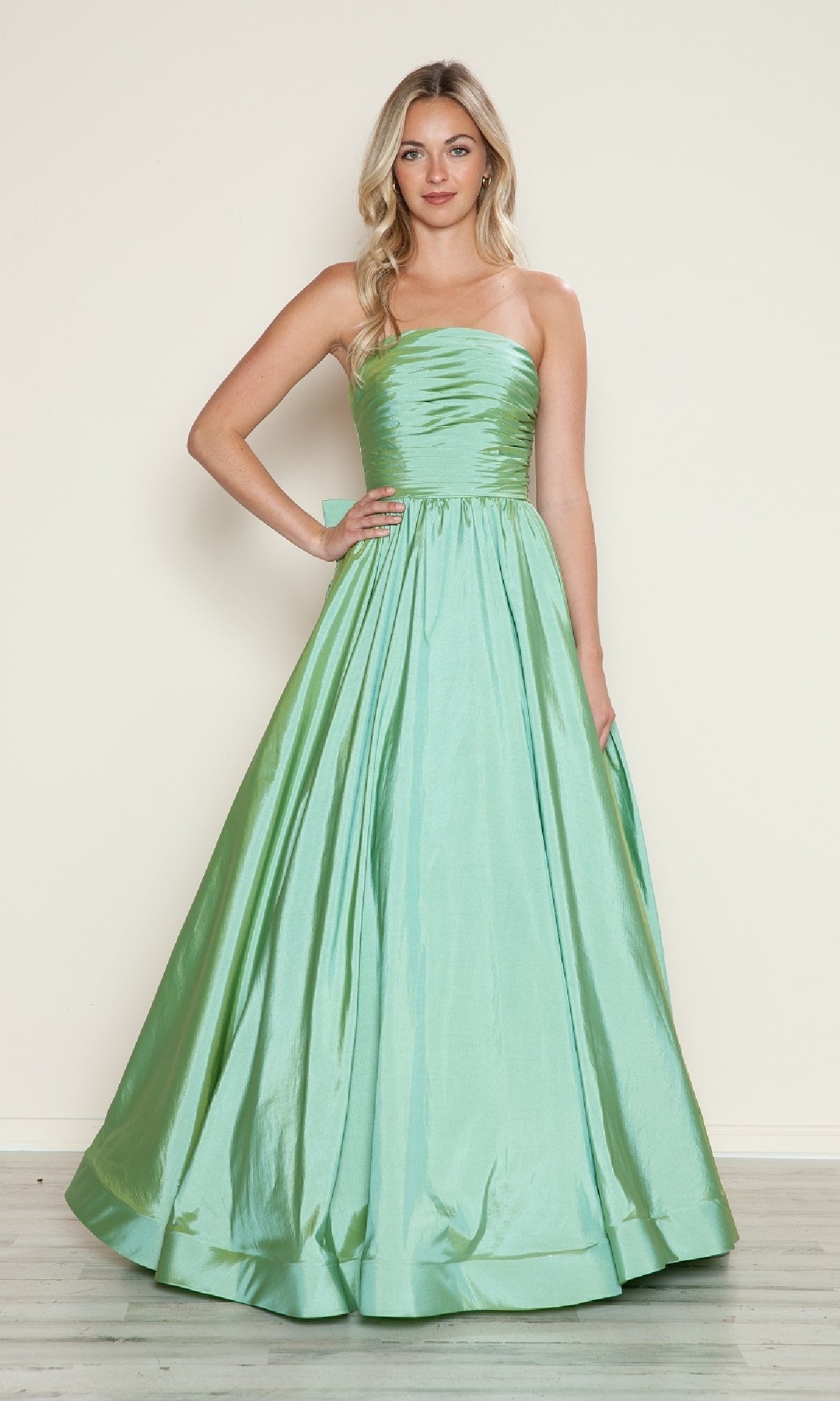Model in Poly USA 9754, a strapless floor-length light green satin prom dress featuring a ruched bodice and adjustable lace-up back, poses against a plain light background.